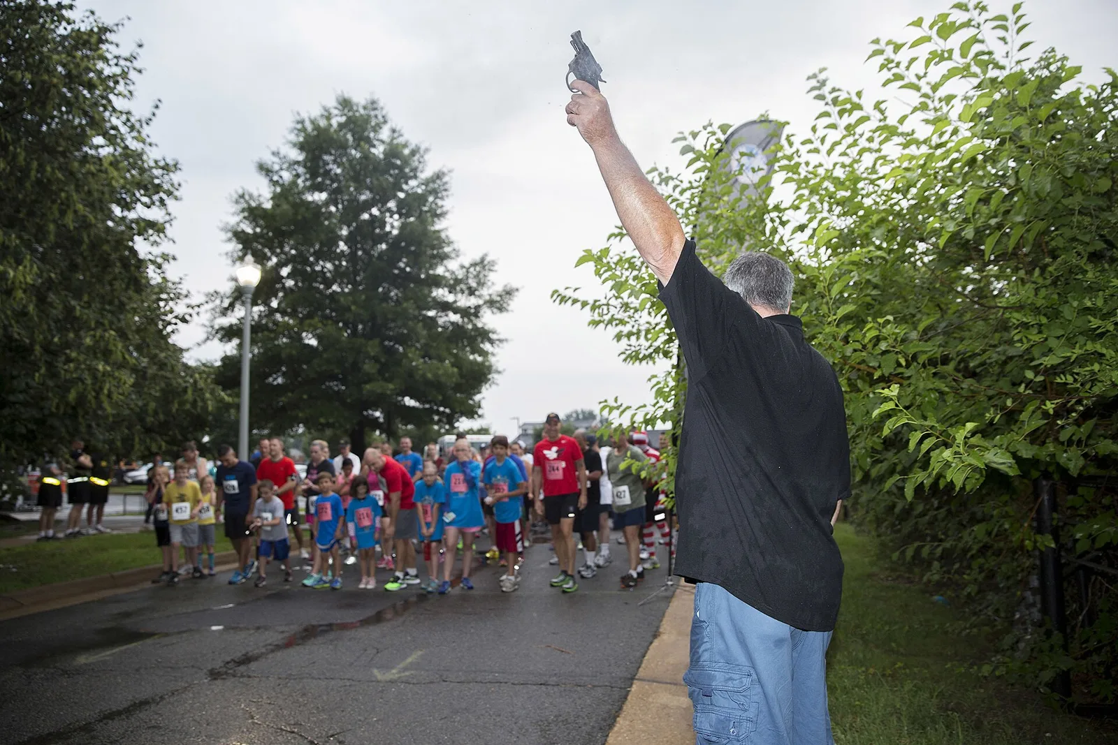 A starter raises the starting pistol over runners and children at the line of a Firecracker 5K at Joint Base Myer-Henderson Hall, Virginia